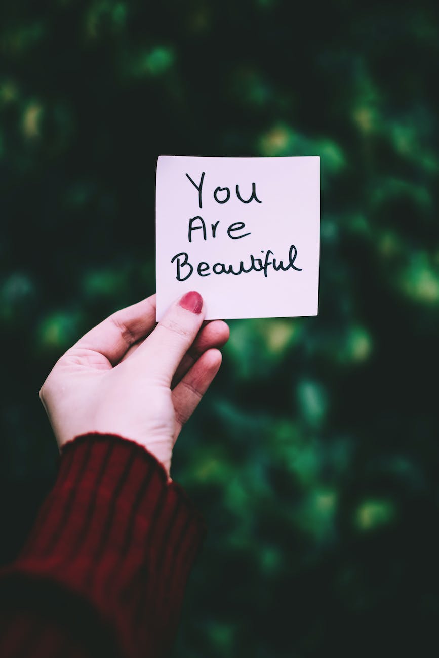 A picture with a female hand holding a sign that says you are beautiful

